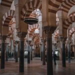Vista interior del famoso Bosque de Columnas de la Mezquita-Catedral de Córdoba. La imagen muestra filas interminables de arcos de herradura bicolores (rojo y blanco) sostenidos por columnas de mármol y jaspe. Cuelgan grandes lámparas de bronce del techo.
