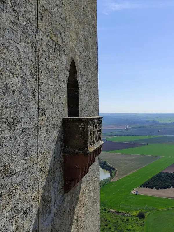 Vista lateral desde un balcón de piedra del Castillo de Almodóvar del Río. El balcón sobresale de la pared de la torre de piedra y tiene una barandilla de hierro forjado.